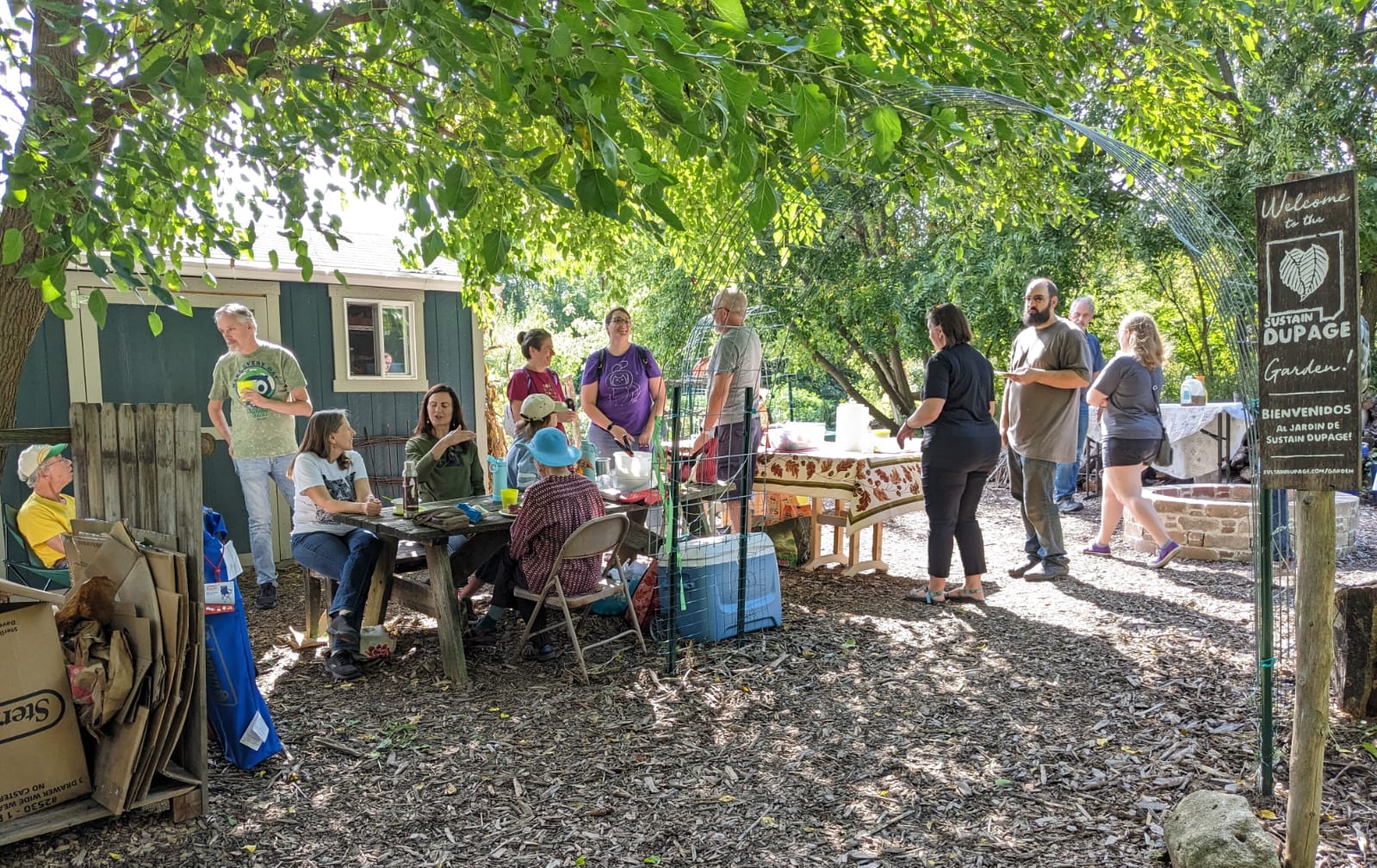 People gathered under the trees near the cabin, Enjoying treats and Community
